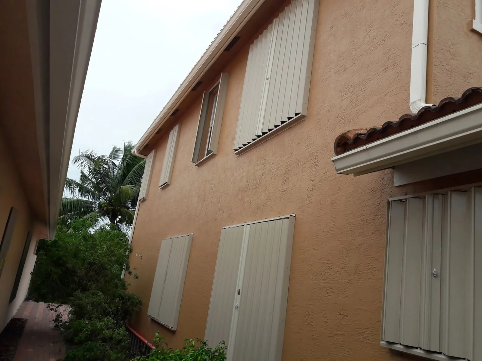 Beige hurricane accordion shutters on a two-story South Florida home